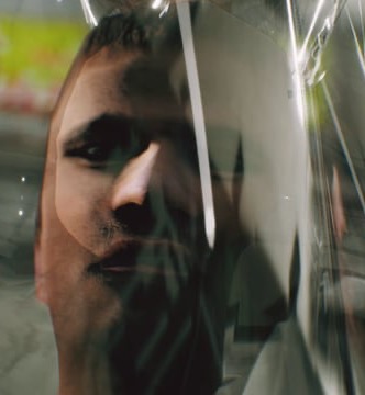 Still from Proxy of Control — a face seen through creased plastic sheeting
