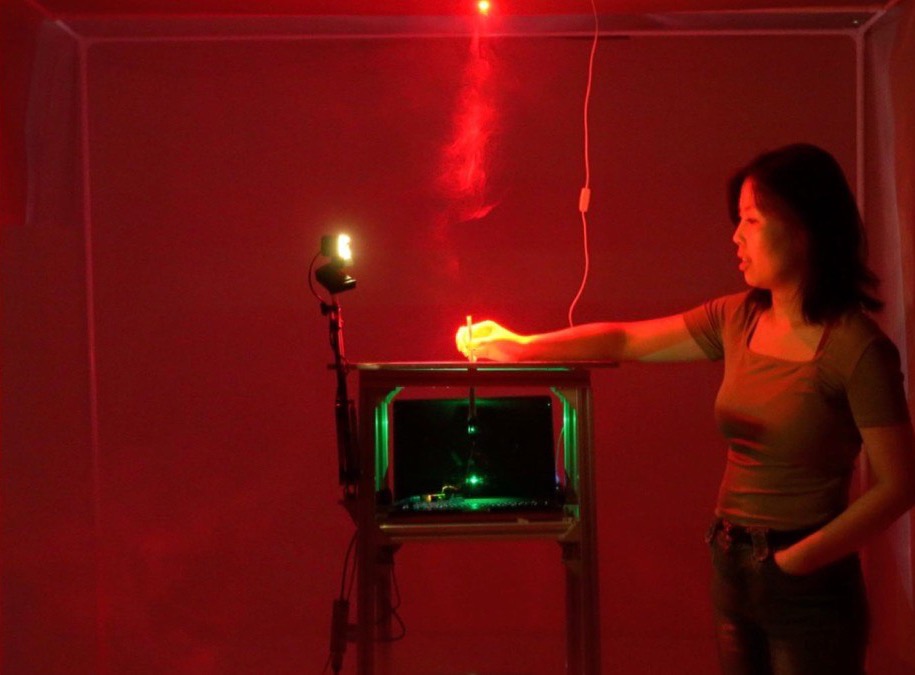 Threads installation — a visitor at a lit plinth in a red room, smoke rising